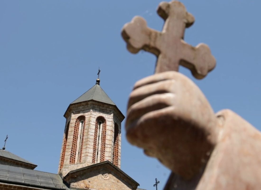 prikaz crkve u manastiru rača i spomenika koji drži pravoslavni krst u ruci